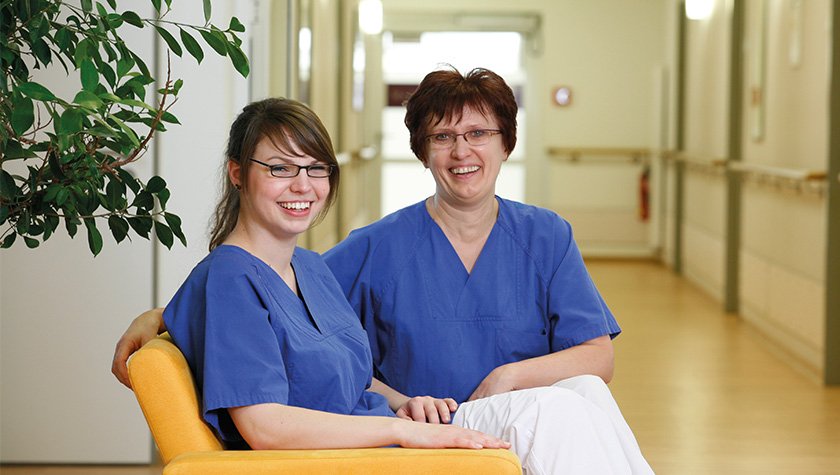 Zwei Pflegerinnen sitzen auf einem sofa in einem Krankenhausflur